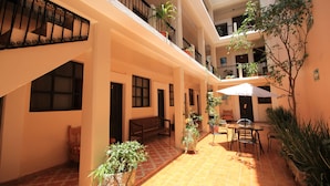 A courtyard with a tiled floor, a bench, potted plants, and outdoor seating.