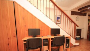A home office with two desks, each with a computer and chair, a wooden staircase, and a clock on the wall.