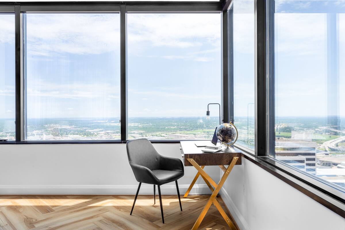 A modern office space with a large window, a black office chair, a wooden desk, and a globe.