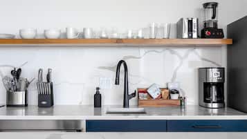A modern kitchen with a marble backsplash, stainless steel appliances, and a wooden shelf above the sink.