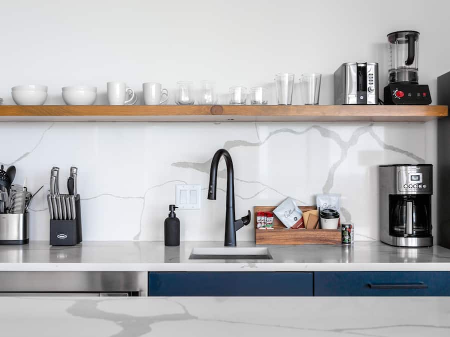 Una cocina moderna con salpicadero de mármol, electrodomésticos de acero inoxidable y un estante de madera sobre el fregadero.