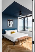 Un dormitorio con cama, ventilador de techo, un ventanal grande y suelo de madera.