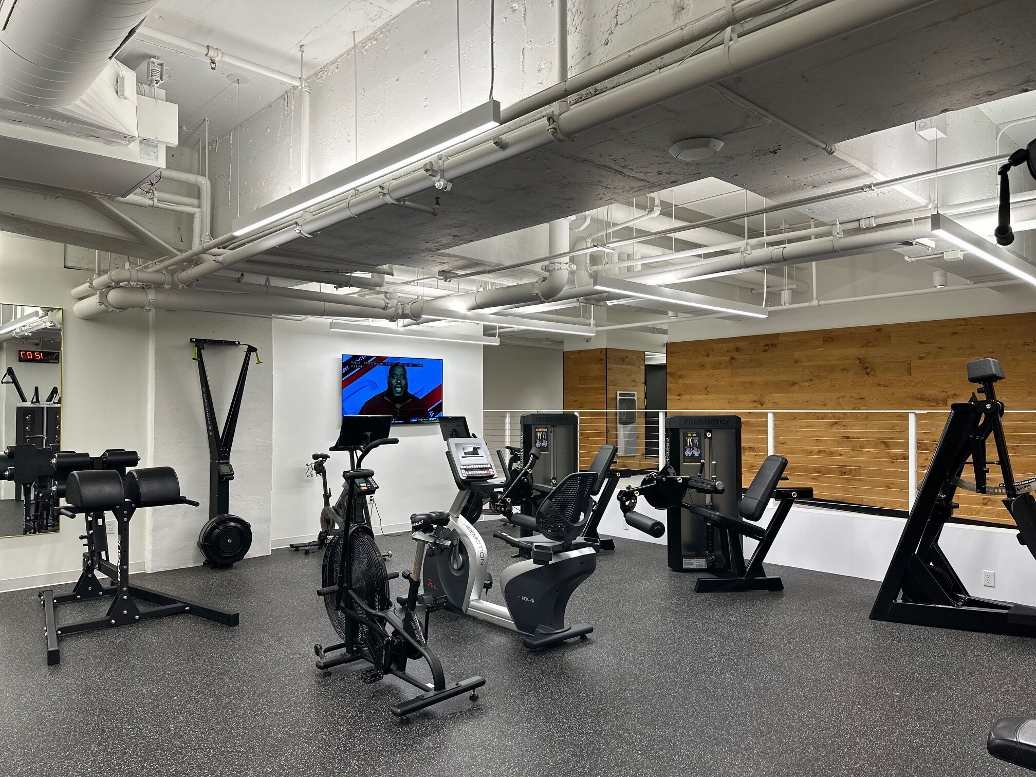 A gym with various exercise equipment, a digital screen, and a wooden wall.