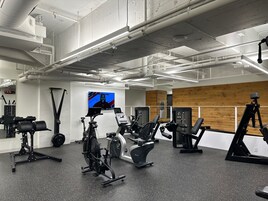 A gym with various exercise equipment, a digital screen, and a wooden wall.
