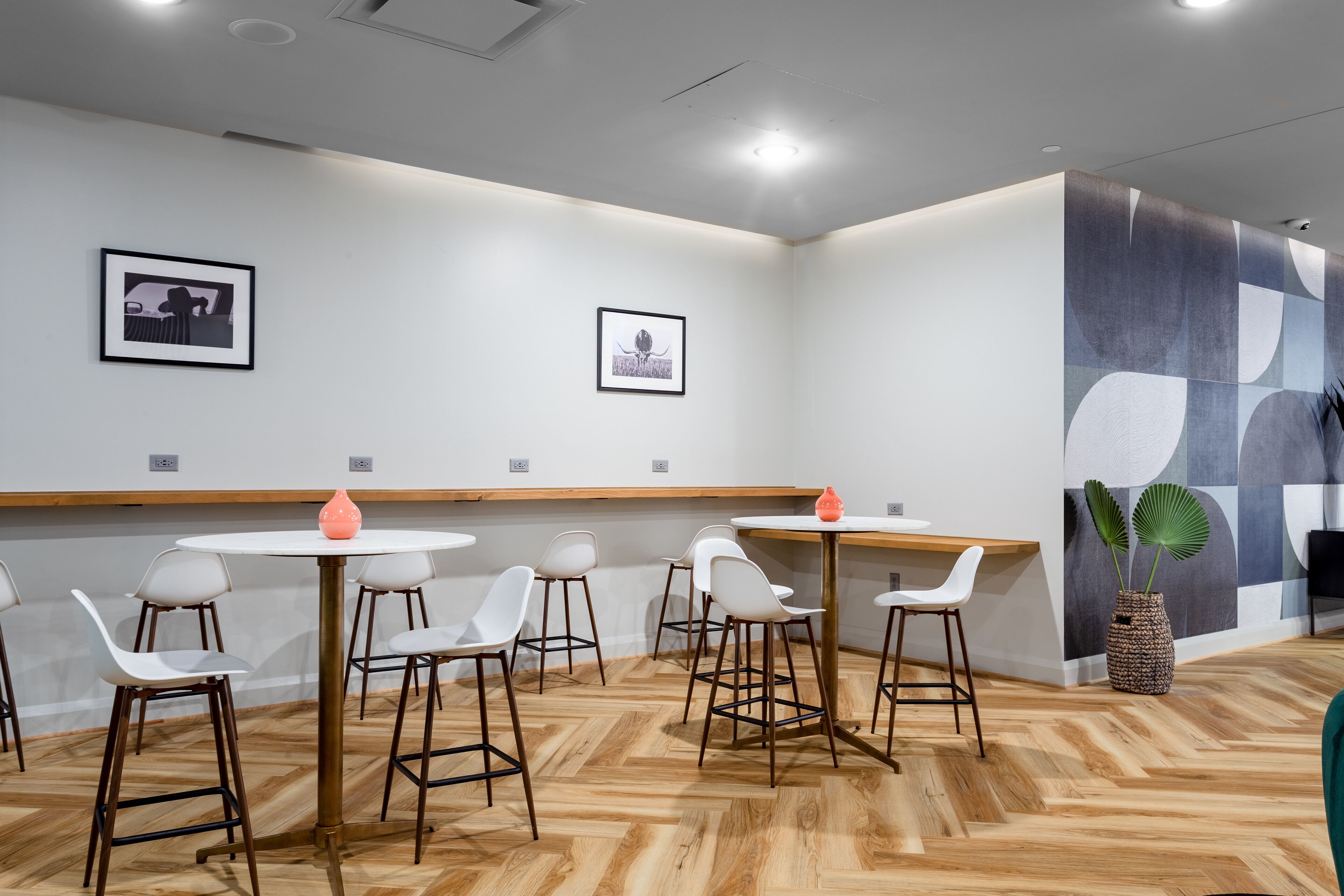 A modern dining area with white chairs and round tables, wooden flooring, and abstract wall art.