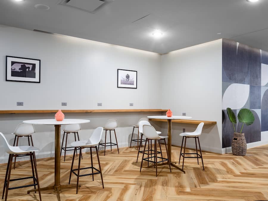 A modern dining area with white chairs and round tables, wooden flooring, and abstract wall art.