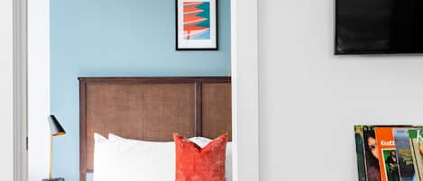 Un dormitorio con cama, ventilador de techo, mesita de noche, lámpara, un cuadro enmarcado, televisor y un armario de madera.