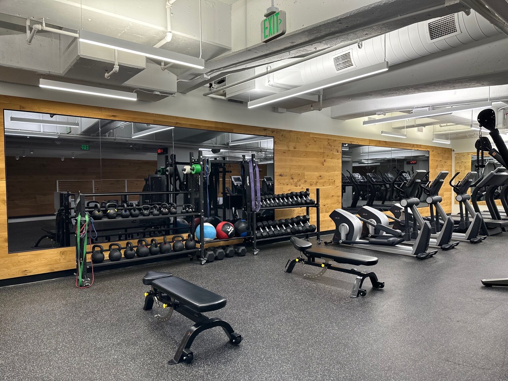 Ein Fitnessraum mit Trainingsgeräten, einer Bank und einer Spiegelwand.