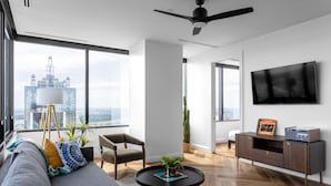 A modern living room with a sofa, chairs, a coffee table, a TV, and a view of a cityscape. - Mint House Dallas Downtown by Kasa (Dallas)