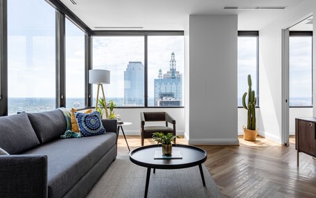 A modern living room with a grey sofa, a round coffee table, and a view of a cityscape through large windows.