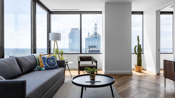 A modern living room with a grey sofa, a round coffee table, and a view of a cityscape through large windows. - Mint House Dallas Downtown by Kasa (Dallas)