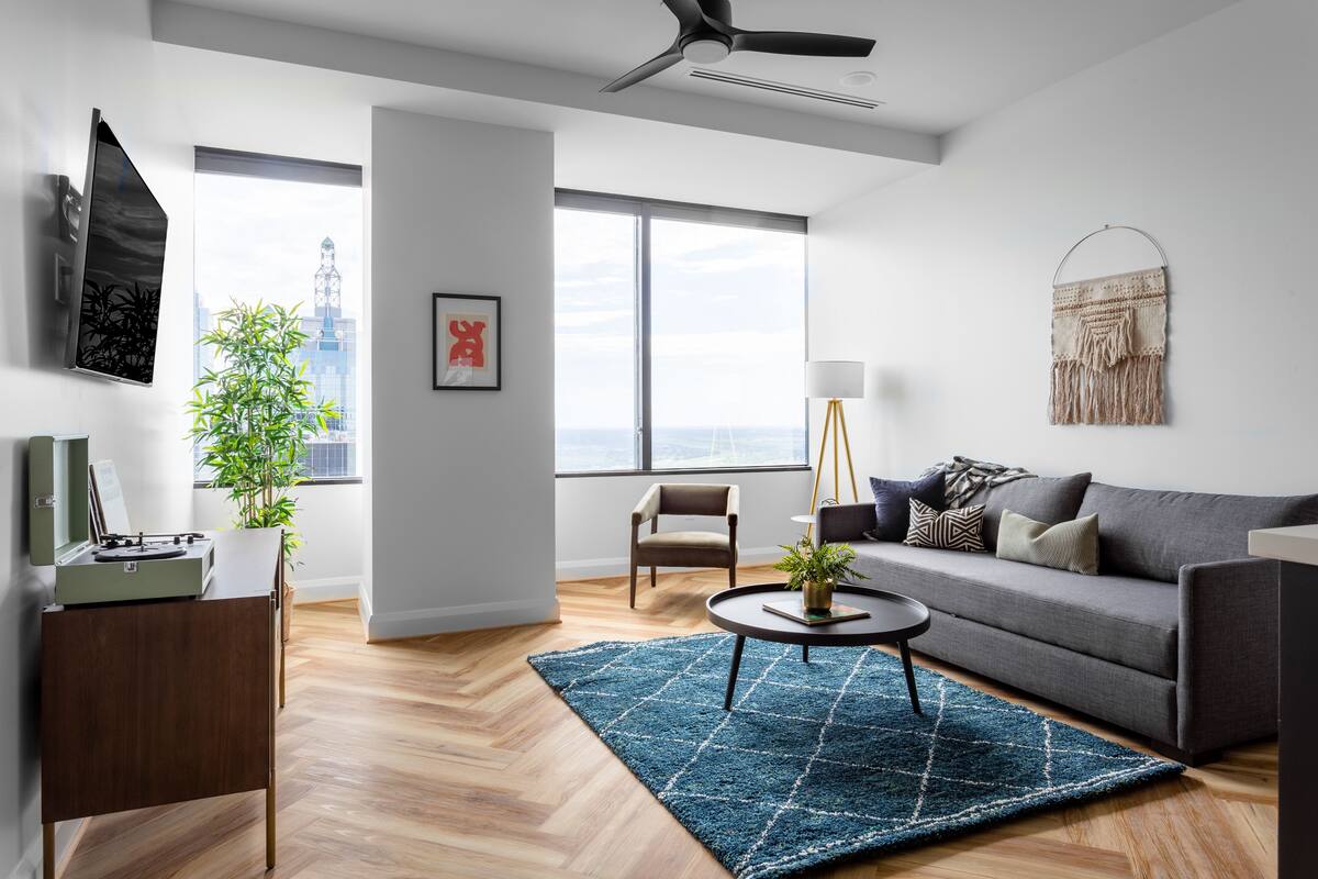 A modern living room with a grey sofa, a coffee table, a floor lamp, and a large window offering a city view.