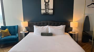 A hotel room with a large bed, two bedside tables with lamps, a blue armchair, and a wall-mounted artwork.