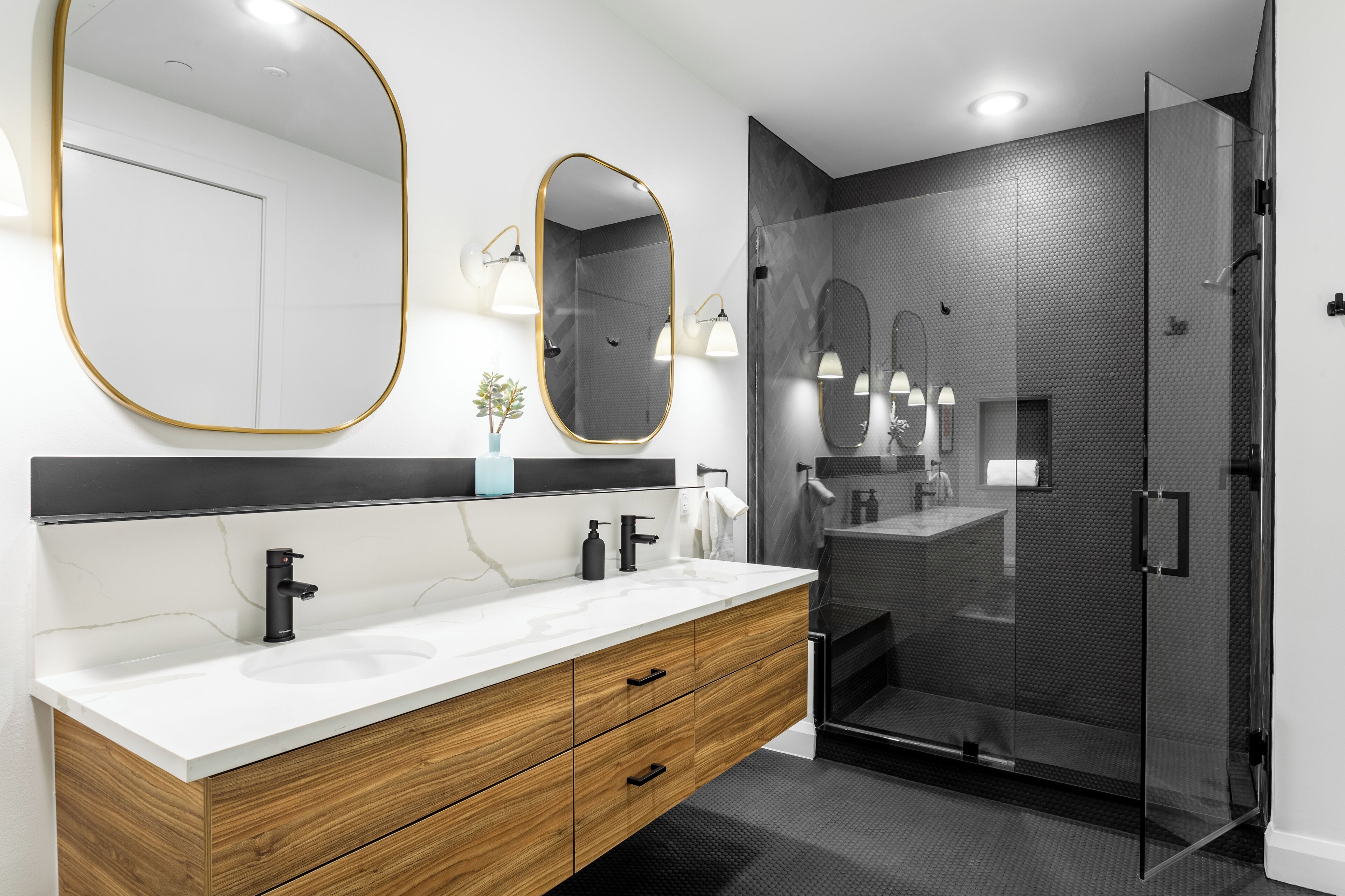 A modern bathroom with a wooden vanity, two mirrors, and a glass shower enclosure.