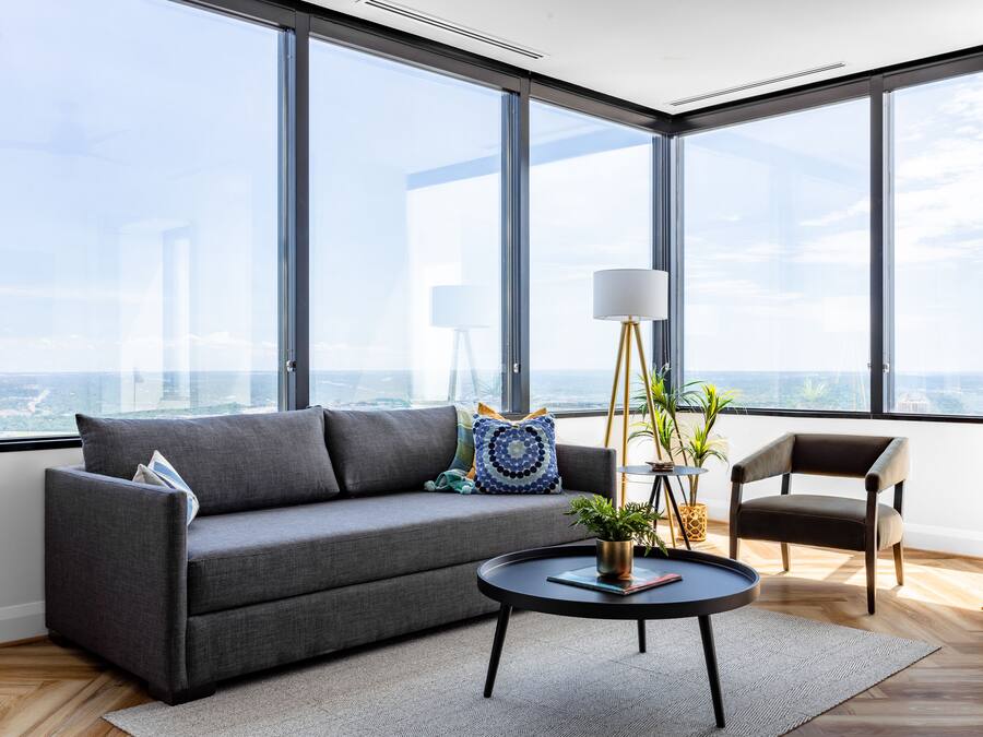 A modern living room with a gray sofa, a round coffee table with a plant, and a view of the city through large windows.