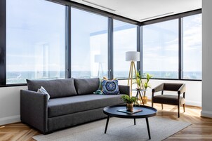 A modern living room with a gray sofa, a round coffee table with a plant, and a view of the city through large windows.