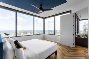 Een moderne slaapkamer met een groot bed, een plafondventilator en een stadszicht door grote ramen.