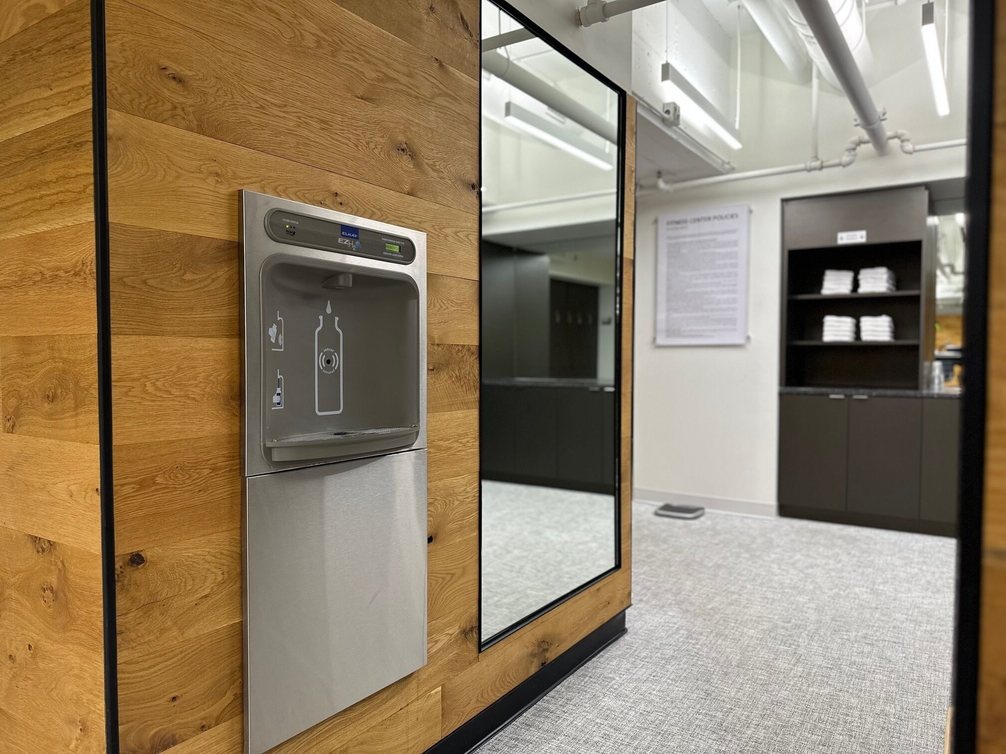 A modern office space with a built-in water dispenser, a wooden wall panel, and a glass partition.