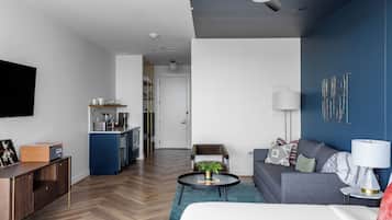 A modern hotel room with a flat-screen TV, a sofa, a dining area, and a kitchen.