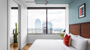A modern hotel room with a large bed, a view of the city skyline, and a cactus plant. - Mint House Dallas Downtown by Kasa (Dallas)