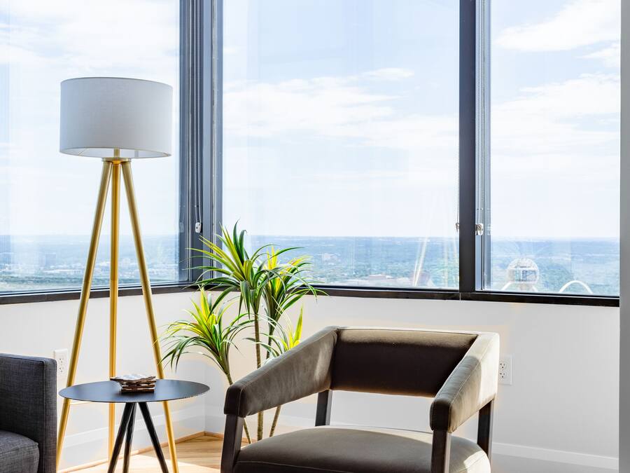 A modern living room with a large window, a floor lamp, a chair, and a small table.