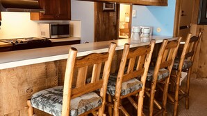 A rustic kitchen with wooden chairs and a wooden bar counter.