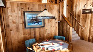 A wooden room with a pool table, two blue chairs, a framed picture on the wall, and a staircase.