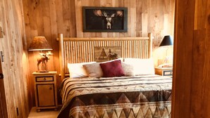 A wooden-paneled room with a bed, a nightstand, a lamp, and a wall-mounted picture.