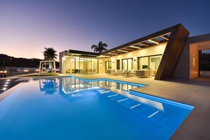 A modern house with a swimming pool, outdoor seating, and a well-lit patio area.