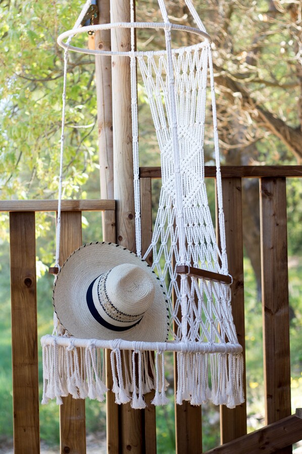 A macrame hanging chair with a straw hat hanging from it.