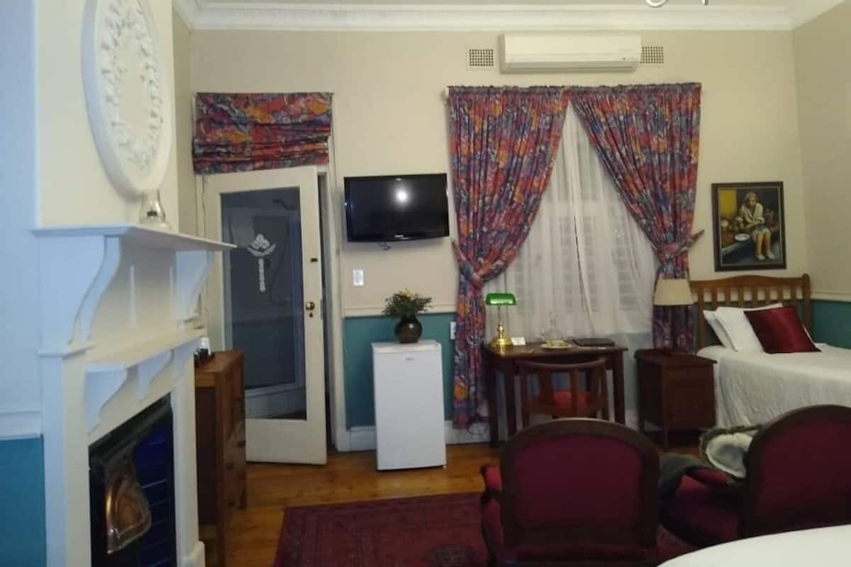 A cozy room with a fireplace, a television, a bed, and a small refrigerator.