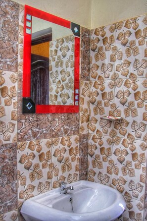 A bathroom with a sink, a mirror, and patterned wall tiles.