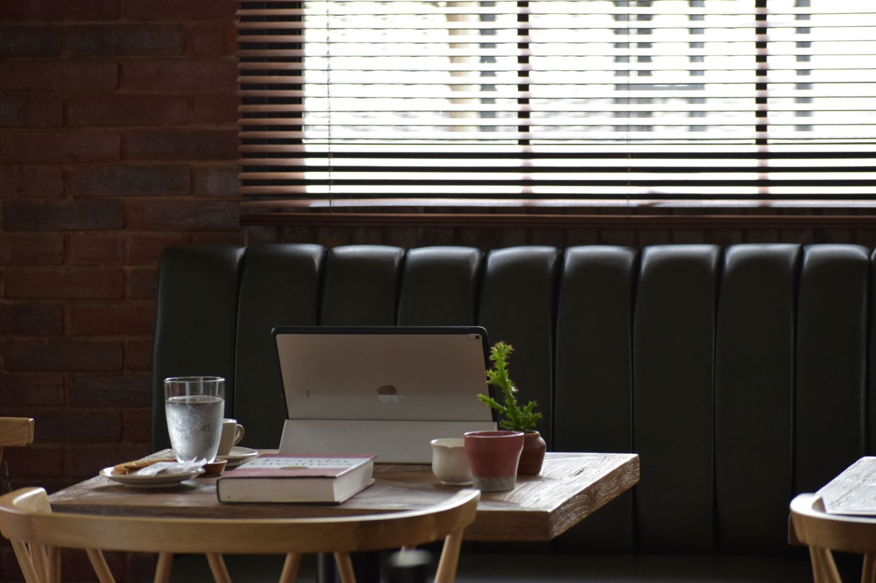 A wooden table with a laptop, a glass of water, a book, and a small potted plant.