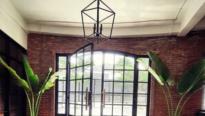 A room with a large open door leading outside, a hanging light fixture, and two large potted plants. - Rumanami Residence (Jakarta)