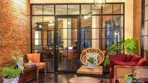 A cozy lounge area with brick walls, a wooden floor, and comfortable seating including a red sofa, a wicker chair, and a brown leather ottoman. - Rumanami Residence (Jakarta)