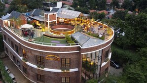A modern building with a rooftop bar and dining area, surrounded by greenery and urban buildings. - Rumanami Residence (Jakarta)