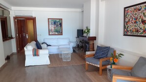 Un salón moderno con un sofá blanco, una mesa de centro de madera y un sillón estampado.