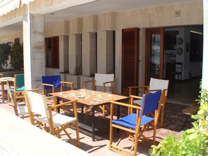 An outdoor patio with wooden tables and chairs, a tiled floor, and a door leading to an interior space. - Fabulous, Ground floor, Pine Walk apartment with large terrace and beach access (Port de Pollença)