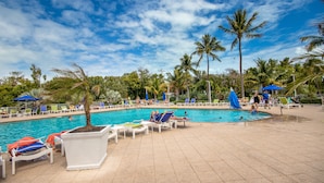 A swimming pool area with lounge chairs and umbrellas, surrounded by palm trees. - Oceanfront Views at Ocean Pointe + Pool + Beach & Marina Access, Updated 2BR (Tavernier)