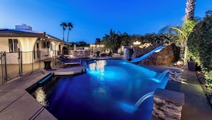 Una piscina con una cascada, rodeada de sillas de descanso y un muro de piedra.