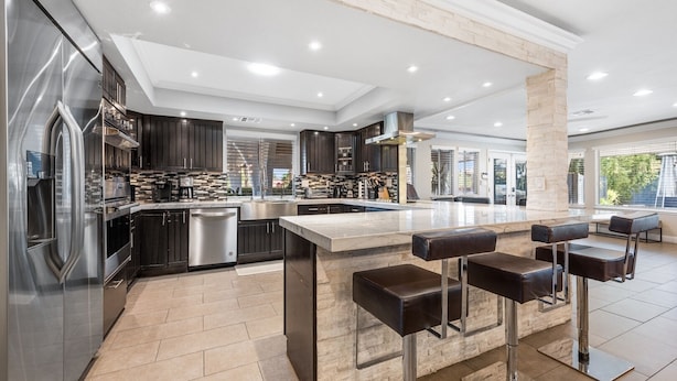Una cocina moderna con armarios oscuros, electrodomésticos de acero inoxidable y una isla central con taburetes de bar.