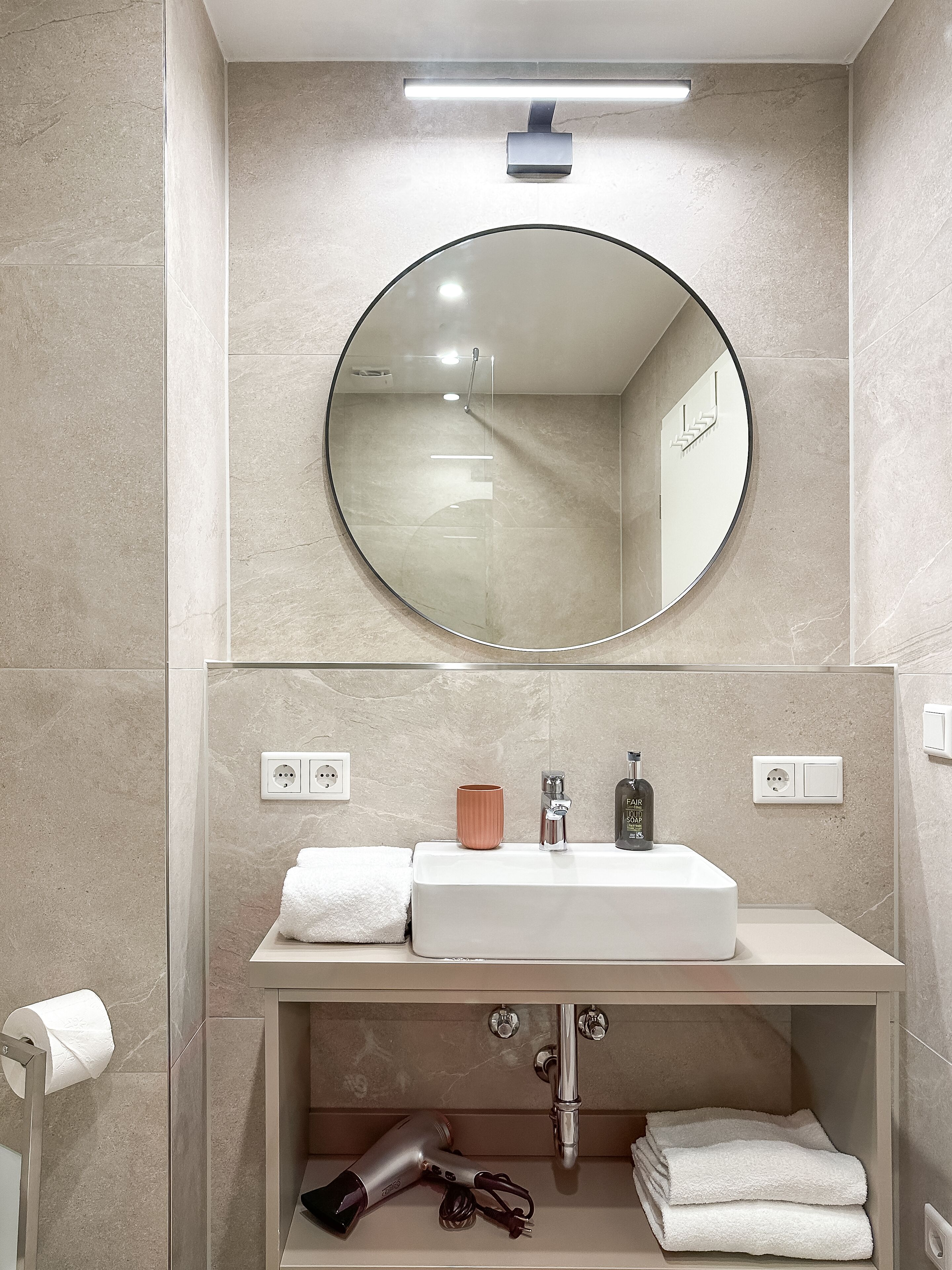 A modern bathroom with a round mirror, a white sink, and a towel rack.