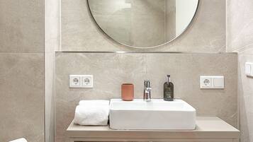 A modern bathroom with a round mirror, a white sink, and a towel rack.