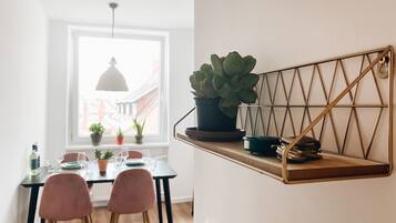 En matplats med ett bord dukat för två personer, en krukväxt på en vägghylla och ett fönster som släpper in naturligt ljus.