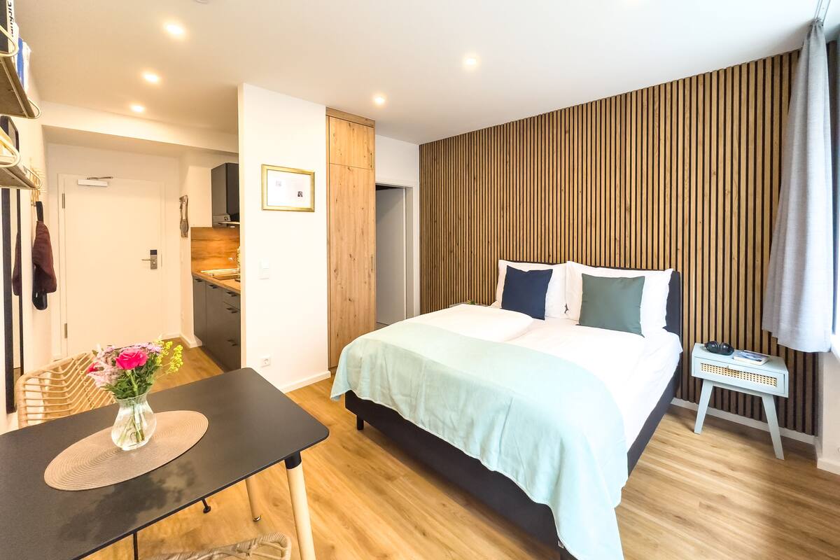 Un dormitorio con cama, mesita de noche y una pequeña mesa con un jarrón de flores.