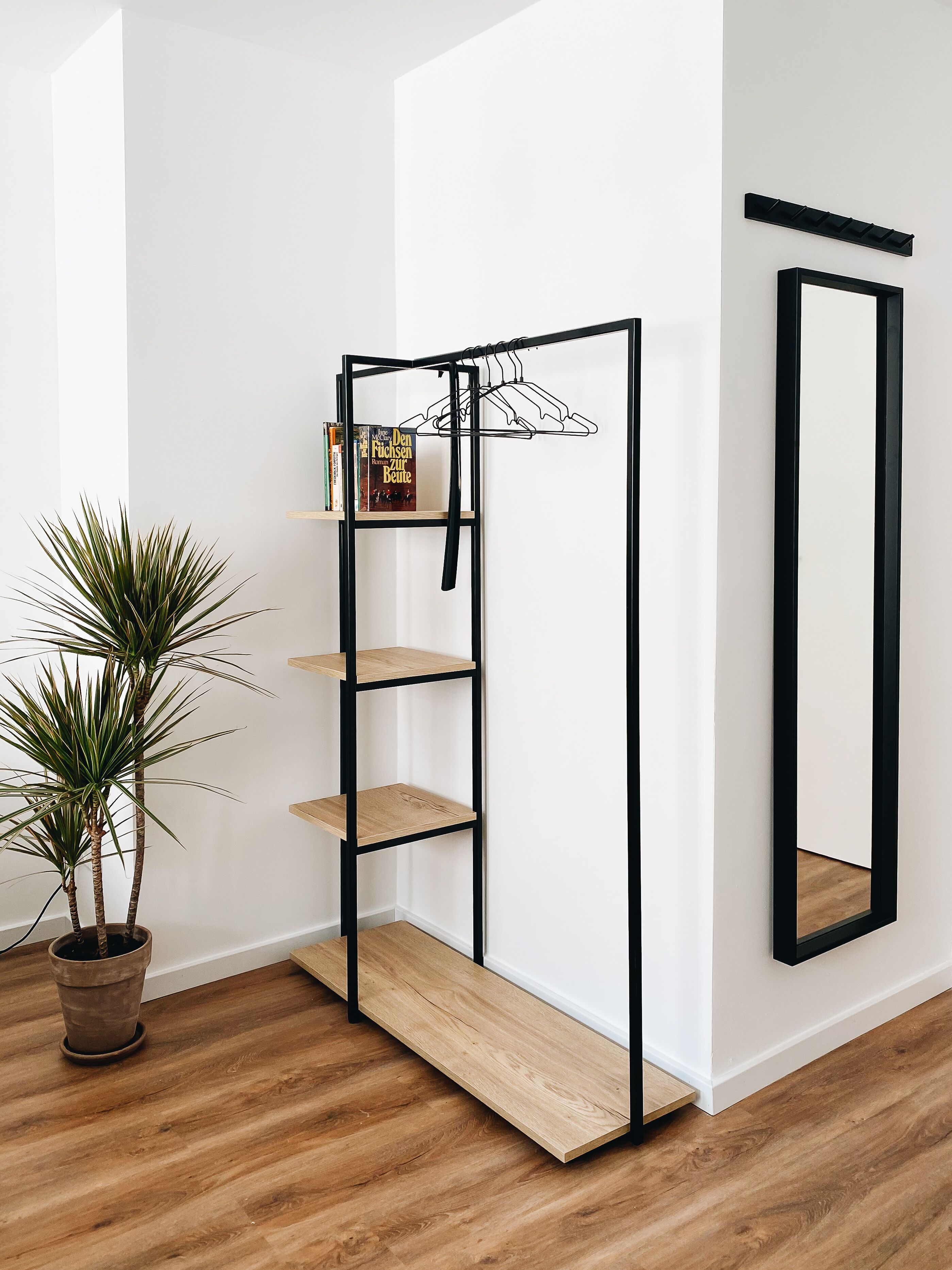 Una habitación minimalista con una estantería de metal negro, una planta en maceta y un espejo en la pared.