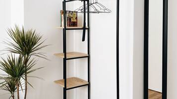 Una habitación minimalista con una estantería de metal negro, una planta en maceta y un espejo en la pared.