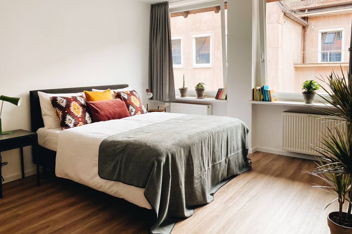 Un dormitorio ordenado con cama, mesita de noche y ventana con plantas.