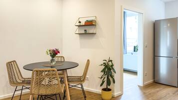 A modern kitchen with a stainless steel refrigerator, a dining area with wicker chairs and a round table, and a potted plant.