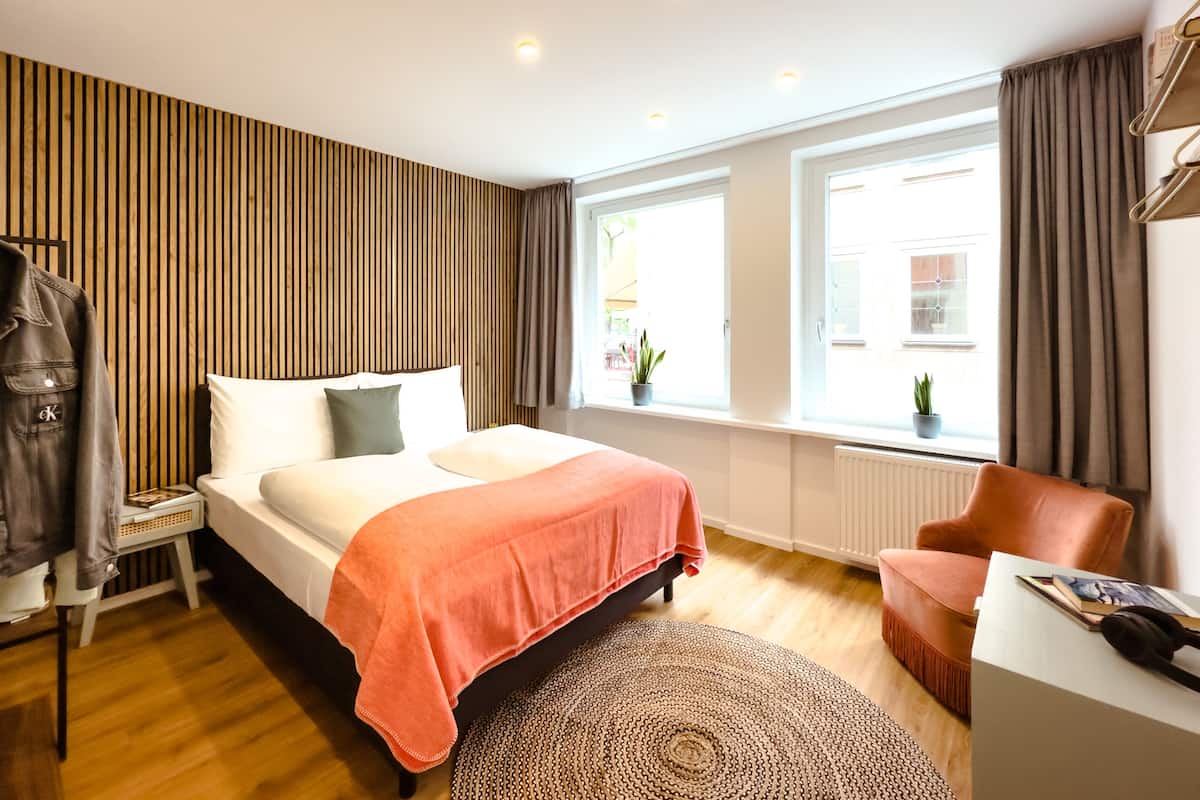 Un dormitorio moderno con una cama, una silla, un escritorio y una ventana con cortinas.
